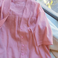 A light pink short-sleeved women's V-neck oversize shirt, sewn using the Longan Craft PDF digital pattern, is displayed on a white surface near a sunlit window.