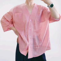 A person models the Women's V-neck Oversize Shirt Sewing Pattern by Longan Craft—a loose, light pink top with two chest pockets and elbow-length sleeves. The PDF digital download paired with black pants and a smartwatch; the face is not shown.