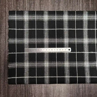 A metal ruler rests on Longon Craft’s Multi Color Plaid Flannel Fabric By The Yard, a comfy polyester-cotton flannelette textile, both set atop a dark wood surface for a cozy autumn vibe.
