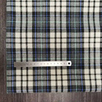 A metal ruler on Longon Craft's Polyester Cotton Plaid Flannel Fabric By The Yard in black, white, blue, and green displays centimeter measurements on a dark wooden surface.
