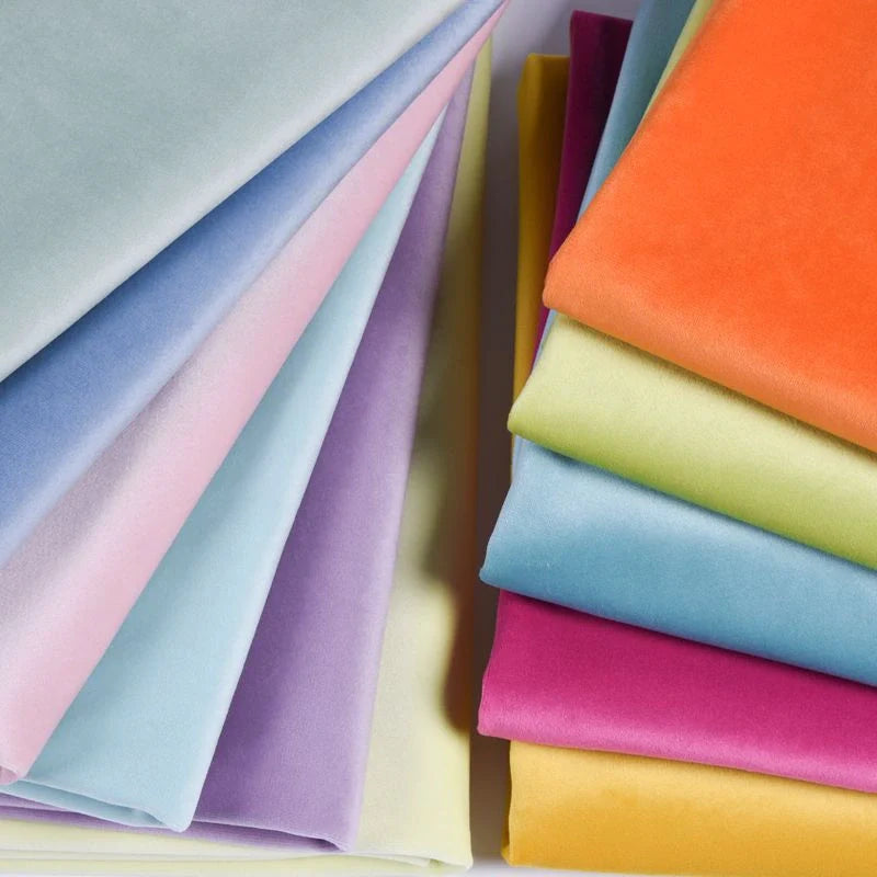 Stacks of fabric in various solid colors, including blue, purple, yellow, orange, green, and pink, arranged in overlapping layers.