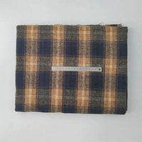 A folded piece of Longan Craft Multicolor Plaid Mammoth Flannel Fabric By The Yard lies on a white background, featuring blue, brown, and beige hues with a metal ruler in centimeters on top for scale.