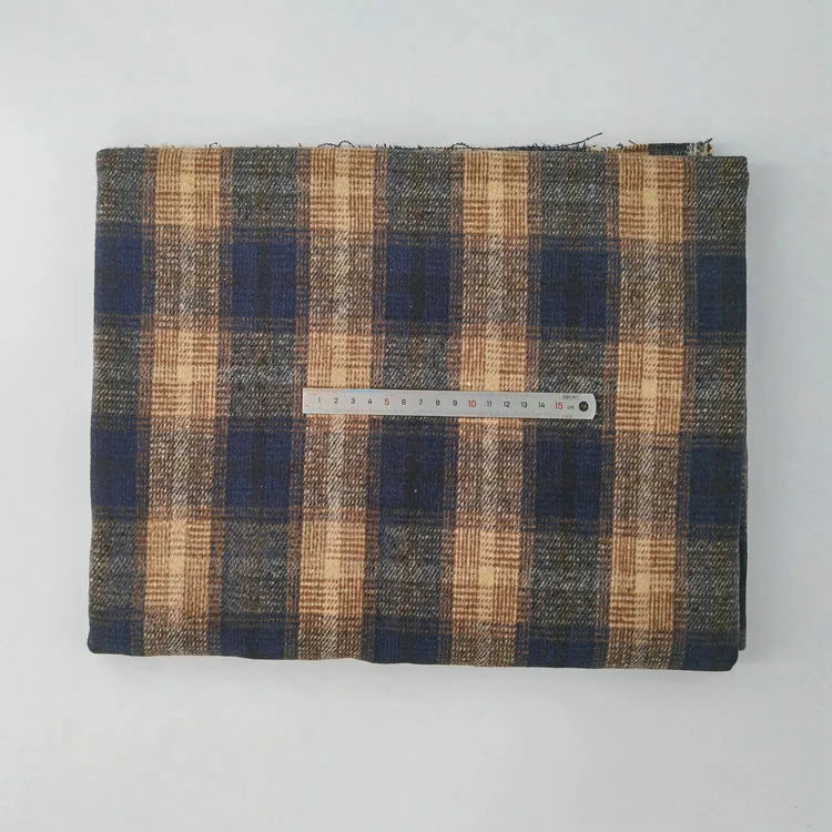 A folded piece of Longan Craft Multicolor Plaid Mammoth Flannel Fabric By The Yard lies on a white background, featuring blue, brown, and beige hues with a metal ruler in centimeters on top for scale.