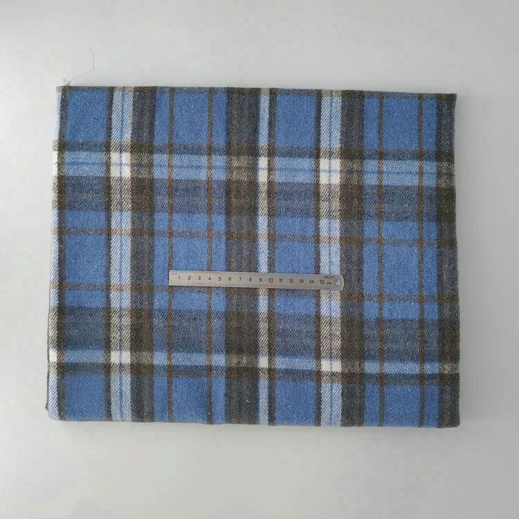 A piece of Multicolor Plaid Mammoth Flannel Fabric by Longan Craft, featuring white, black, and brown stripes on blue, is folded under a metal ruler laid horizontally across its center on a light surface.