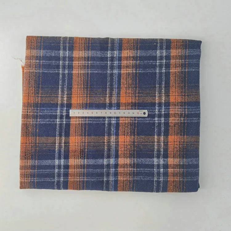 A piece of Longan Craft Multicolor Plaid Mammoth Flannel Fabric by the yard in blue, orange, and white rests on a white surface with a ruler across it for scale; brushed polyester cotton flannelette, perfect for shirts.