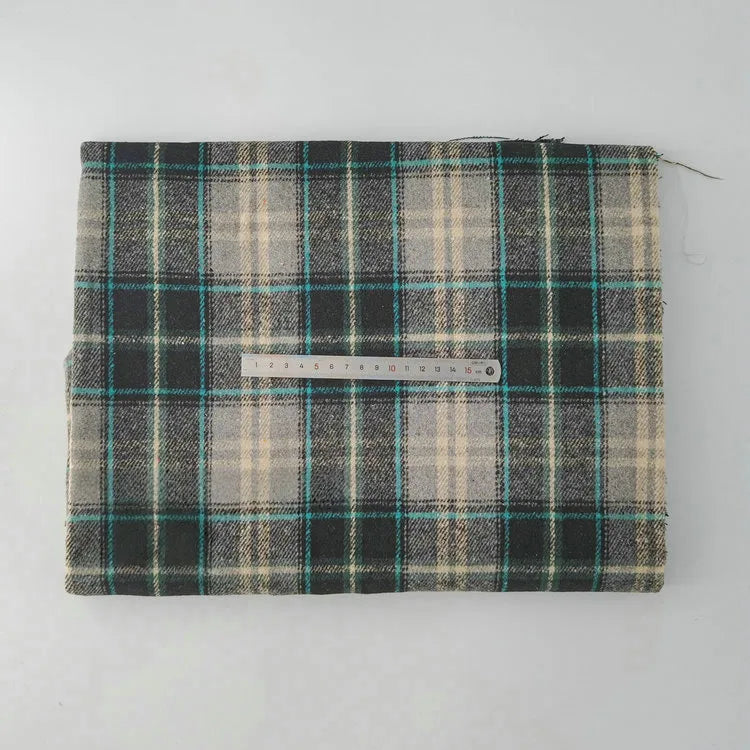A folded piece of Longan Craft Multicolor Plaid Mammoth Flannel Fabric by the yard is laid flat on a white surface, showing green, black, beige, and teal plaid with a 15 cm metal ruler on top for scale.