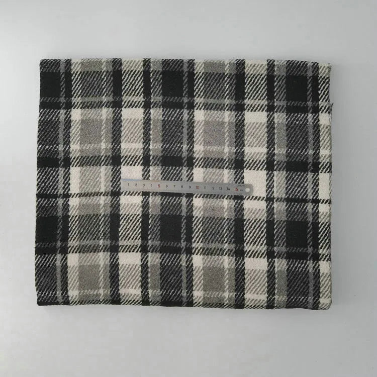 A piece of Longan Craft Multicolor Plaid Mammoth Flannel Fabric By The Yard lies folded on a flat surface, displaying its black, white, and gray brushed polyester cotton material with a clear ruler on top for scale.