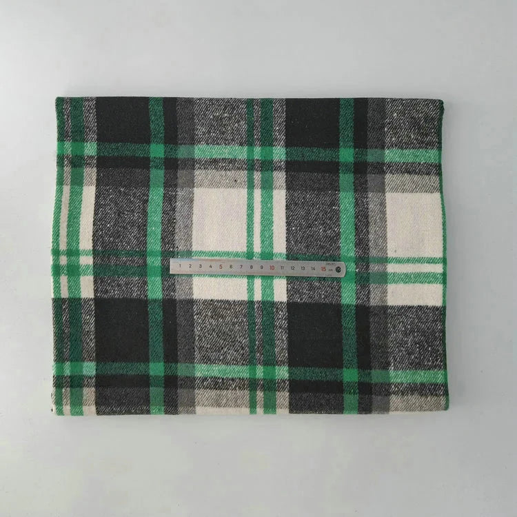 The Longan Craft Multicolor Plaid Mammoth Flannel Fabric By The Yard, a brushed polyester-cotton flannelette ideal for shirts, is shown neatly folded in green, black, and white plaid with a metal ruler for scale against a light gray background.