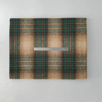 A folded piece of Multicolor Plaid Mammoth Flannel Fabric by Longan Craft is displayed on a white surface with a metal ruler on top for scale, showing its soft brushed polyester cotton texture—ideal for shirts and crafts.