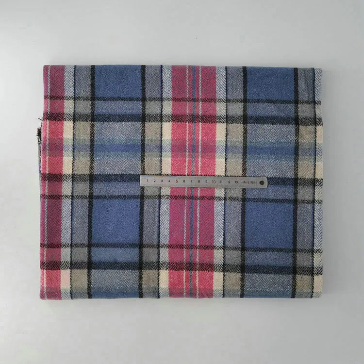 A folded piece of Longan Craft Multicolor Plaid Mammoth Flannel Fabric by the yard lies on a white surface with a metal ruler on top, showing its blue, red, beige, and black brushed polyester cotton blend plaid pattern.