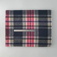 A folded Longan Craft Multicolor Plaid Mammoth Flannel Fabric by the yard, in navy, red, grey, and cream tones, lies on a white surface with a metal ruler across the middle for scale.