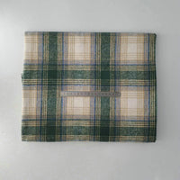A folded Longan Craft Multicolor Plaid Mammoth Flannel Fabric by the yard rests on a white surface with a metal ruler for scale, showing its green, beige, and blue brushed polyester cotton textile, perfect for comfy shirts.