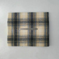 A folded Multicolor Plaid Mammoth Flannel Fabric by Longan Craft in beige, black, and blue rests on a white surface with a metal ruler laid horizontally across the center for scale.