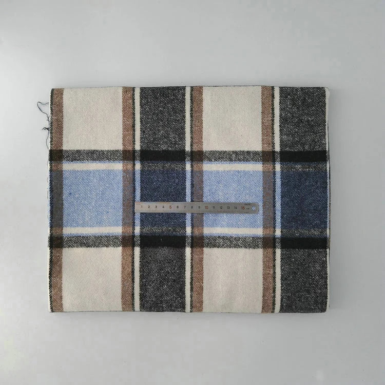 A folded Multicolor Plaid Mammoth Flannel Fabric by Longan Craft lies on a light surface with a metal ruler showing its size. The comfy brushed polyester cotton flannelette features black, brown, blue, and cream tones—great for shirts.