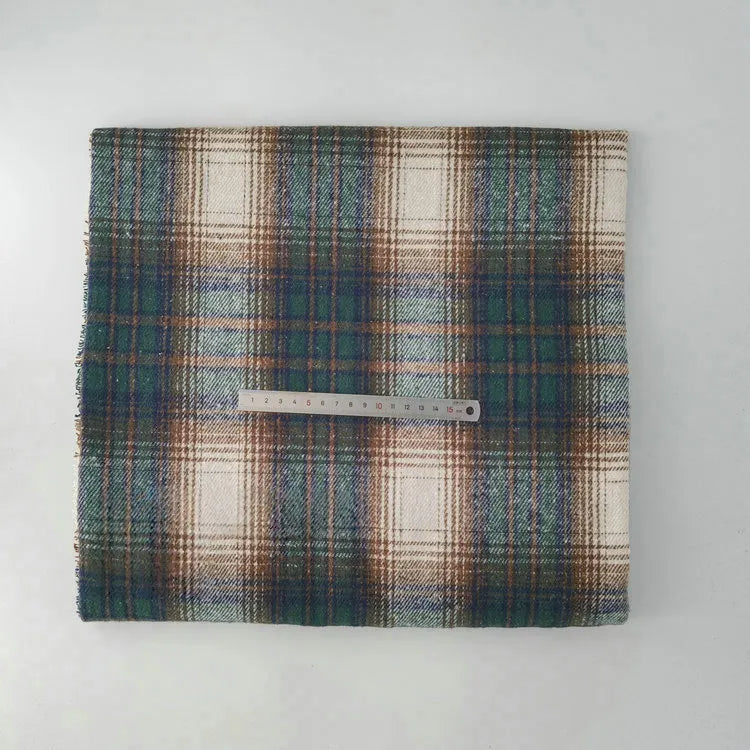 A piece of Longan Craft Multicolor Plaid Mammoth Flannel Fabric by the yard is folded with a metal ruler across its width, showing green, brown, and cream tones on a white background. Brushed polyester cotton flannelette—ideal for shirts.