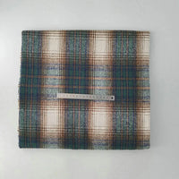 A piece of Longan Craft Multicolor Plaid Mammoth Flannel Fabric by the yard is folded with a metal ruler across its width, showing green, brown, and cream tones on a white background. Brushed polyester cotton flannelette—ideal for shirts.