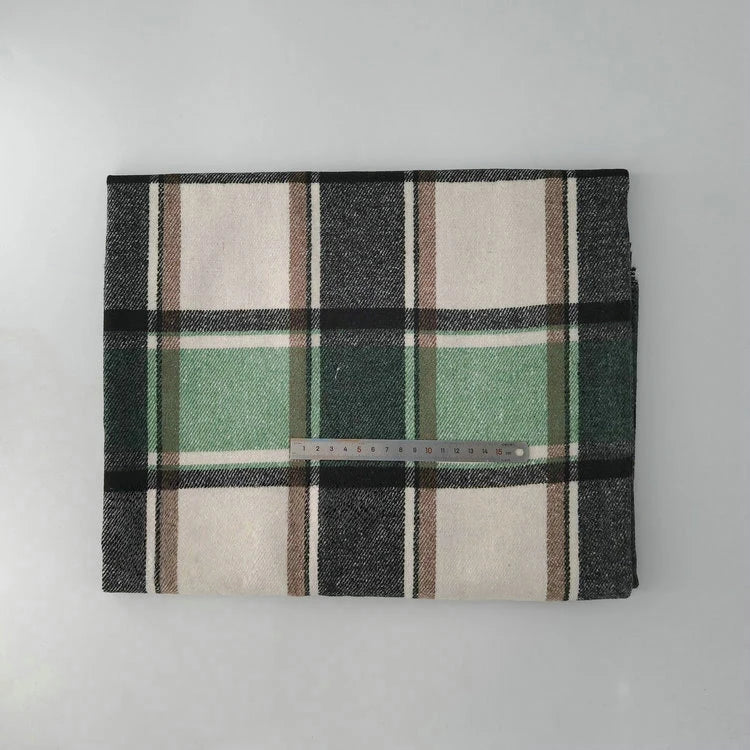 The Multicolor Plaid Mammoth Flannel Fabric by Longan Craft is shown folded with large black, white, brown, and green checks. A center ruler shows scale. This brushed polyester cotton flannel is displayed on a light gray background.