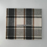 A folded piece of Longan Craft Multicolor Plaid Mammoth Flannel Fabric by the yard, made of brushed polyester cotton, is shown in black, brown, beige, and white tones with a clear plastic ruler on top for scale.