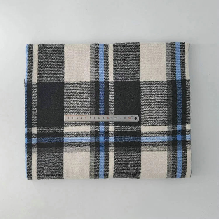 A piece of Longan Craft Multicolor Plaid Mammoth Flannel Fabric by the yard, featuring black, white, gray, and blue stripes, is displayed folded on a flat surface with a clear ruler on top to show its size.