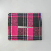 A folded Multicolor Plaid Mammoth Flannel Fabric by Longan Craft with a transparent ruler placed across its center is displayed on a plain light gray surface.
