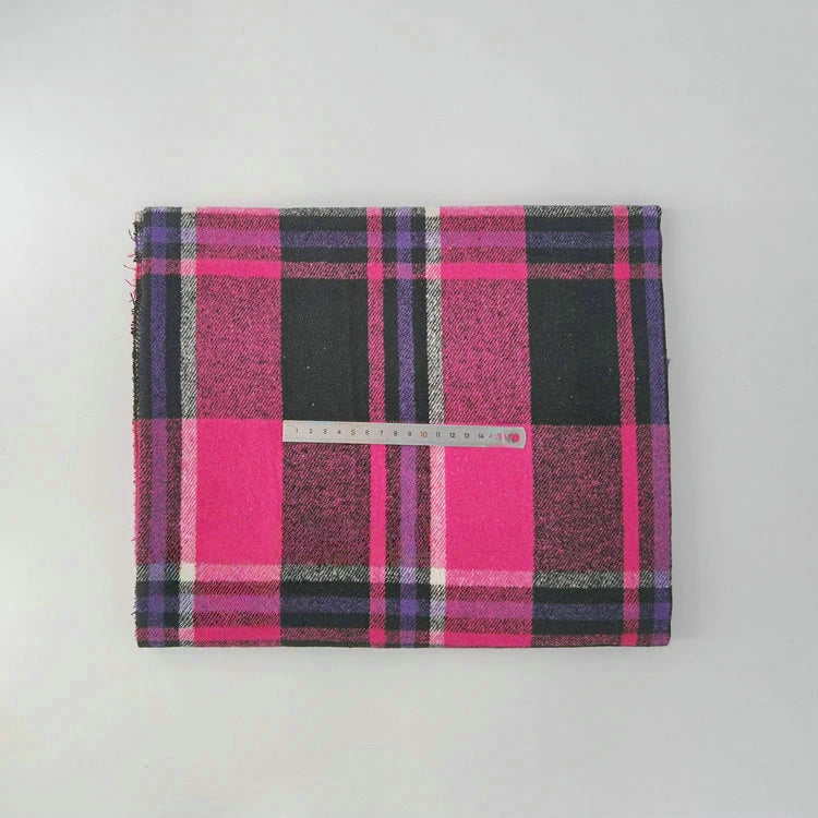 A folded Multicolor Plaid Mammoth Flannel Fabric by Longan Craft with a transparent ruler placed across its center is displayed on a plain light gray surface.