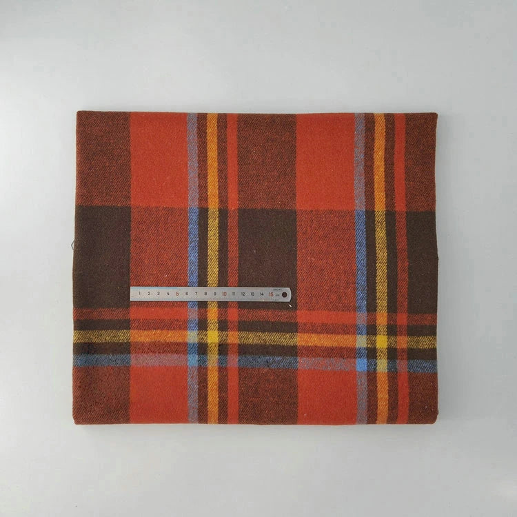 A folded Multicolor Plaid Mammoth Flannel Fabric by Longan Craft rests on a white surface, with a metal ruler on top for scale. This soft brushed polyester cotton flannelette is perfect for shirts and available by the yard.