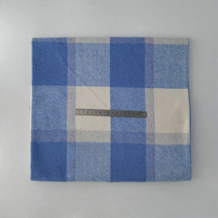 A steel ruler rests atop Longan Craft’s Multicolor Plaid Mammoth Flannel Fabric by the yard, a comfy brushed polyester-cotton flannelette textile for shirts, shown folded on a light surface.