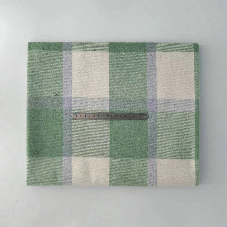A folded Multicolor Plaid Mammoth Flannel Fabric by Longan Craft is displayed on a flat surface with a metal ruler laid across it to show scale. This brushed polyester cotton textile is ideal for comfy shirts and sold by the yard.