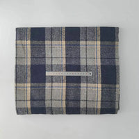 A folded piece of Longan Craft Multicolor Plaid Mammoth Flannel Fabric rests on a white surface, with a silver ruler lying horizontally across the center. This brushed polyester-cotton textile is ideal for comfy shirts.