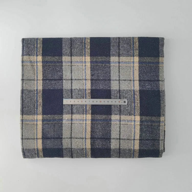 A folded piece of Longan Craft Multicolor Plaid Mammoth Flannel Fabric rests on a white surface, with a silver ruler lying horizontally across the center. This brushed polyester-cotton textile is ideal for comfy shirts.