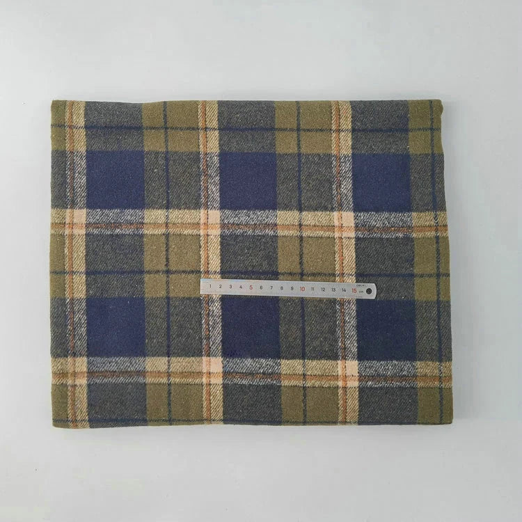 A piece of Multicolor Plaid Mammoth Flannel Fabric By The Yard from Longan Craft, in olive green, navy blue, and beige stripes, is folded on a white surface with a 15-cm ruler on top to show scale.