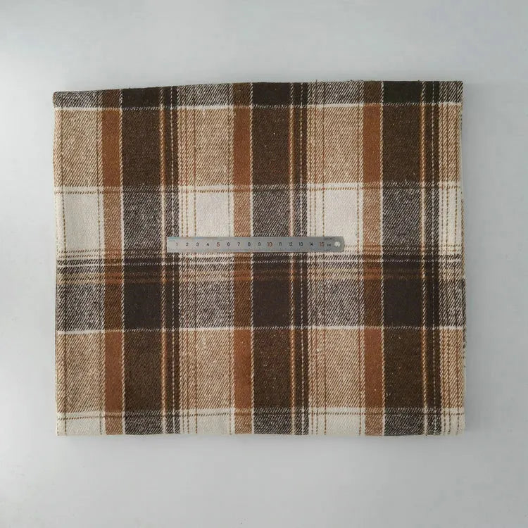 A piece of Longan Craft Multicolor Plaid Mammoth Flannel Fabric by the yard is displayed on a white surface with a metal ruler for scale, showing its brown, beige, and cream checked brushed polyester cotton flannelette.