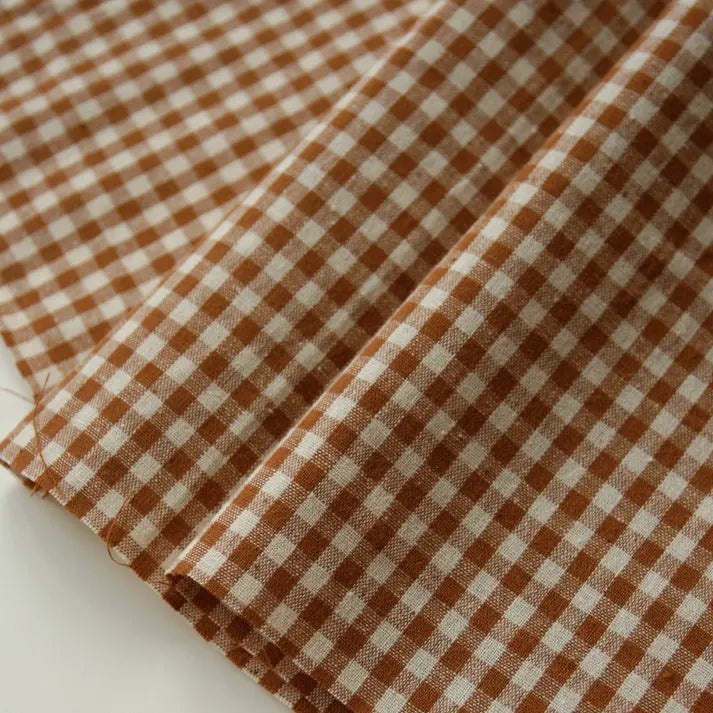 Close-up of the Longan Craft 100% Cotton Gingham Poplin Fabric By The Yard, featuring a classic brown and white multicolor yarn-dyed checkered pattern with evenly spaced squares. The premium soft poplin material is laid flat, highlighting its distinctive texture and weave—ideal for garment making.