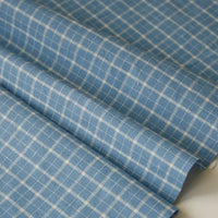 The 100 Cotton Gingham Poplin Fabric By The Yard from Longan Craft features a multicolor yarn-dyed checkered pattern, displayed here in blue and white gentle folds under natural light. This premium soft poplin material appears smooth and lightweight, making it ideal for garment making such as shirts or dresses.