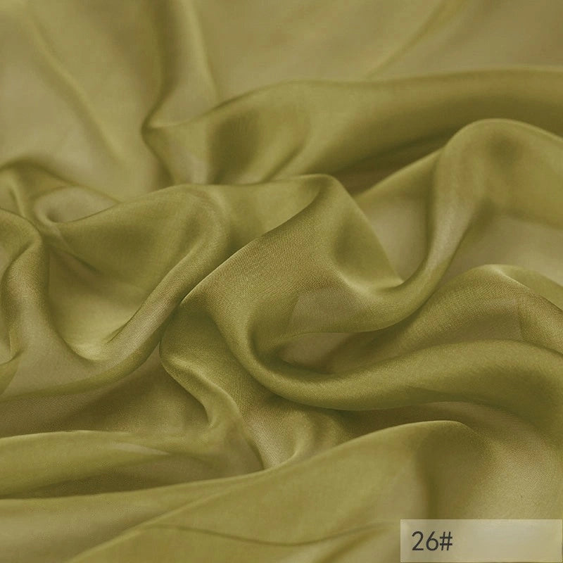 Light olive green, sheer, and softly crumpled 100 Mulberry Silk Chiffon Fabric by Longan Craft with a smooth texture. The lower right corner features a small label marked 26#. Ideal lightweight chiffon material for dresses.