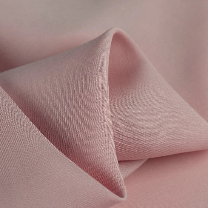 A close-up of Longan Craft's 100% rayon fabric by the yard in light pink shows its smooth, silky texture and gentle folds—ideal soft viscose material for dressmaking and clothing projects.