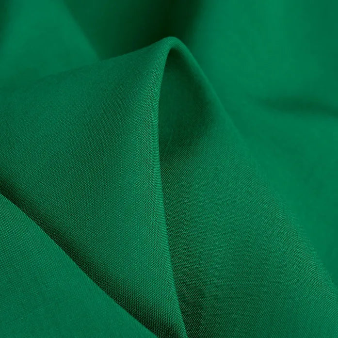 A close-up of Longan Craft's 100 Rayon Fabric By The Yard reveals its vibrant green color, lightweight softness, and smooth texture—ideal as a breathable, solid color viscose material for comfortable dressmaking and clothing projects.