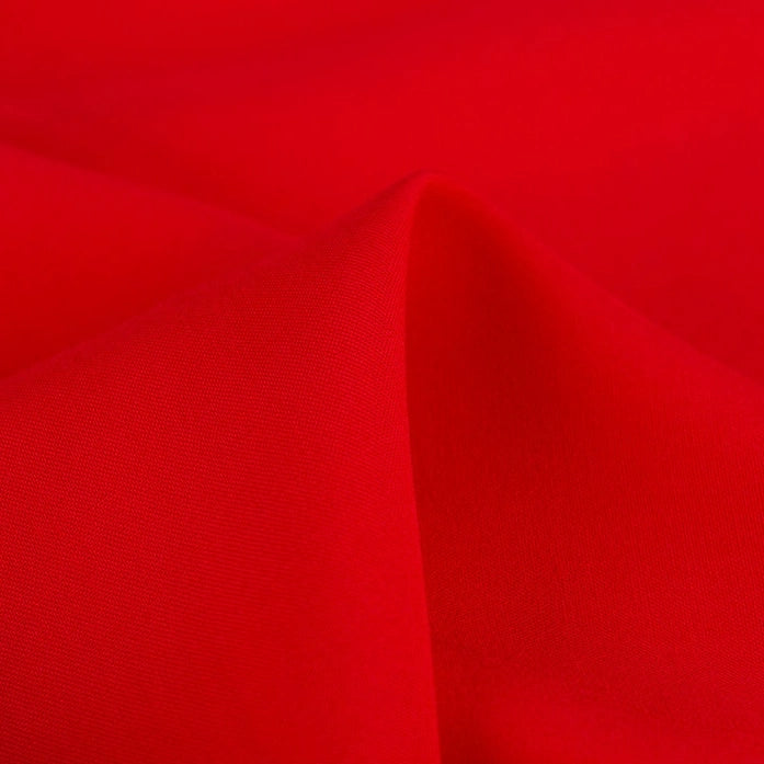A close-up of Longan Craft's 100% rayon fabric by the yard shows its smooth, vibrant red viscose material with soft folds and gentle shadows, highlighting the texture perfect for dressmaking and solid color clothing projects.