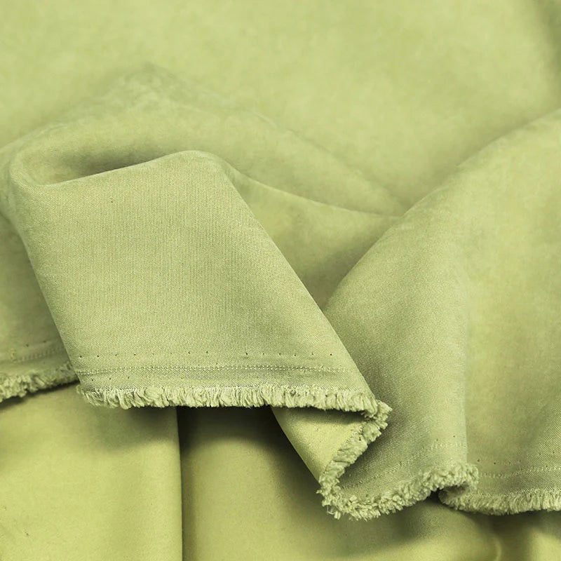 Longan Craft’s Multi Color Microsuede Polyester Peachskin Fabric by the yard features a soft, brushed peach skin texture with a cozy feel—displayed here in light green, draped and slightly folded to show its subtle fringe edge.