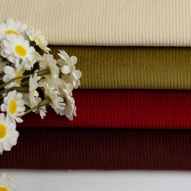 Four stacked pieces of Longan Craft 11 Wales Cotton Corduroy Fabric by the yard in cream, olive green, red, and burgundy shades, with white and yellow artificial daisies arranged on the left side.