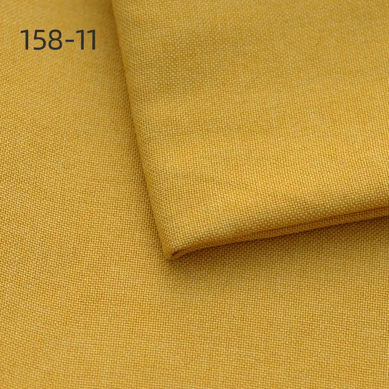 Close-up of Longan Craft Faux Linen Upholstery Fabric in mustard yellow, featuring a fine textured weave. A folded piece rests on top. Product code 158-11 is shown in the upper left corner. Ideal for reupholstering chairs, sofas, and curtains.