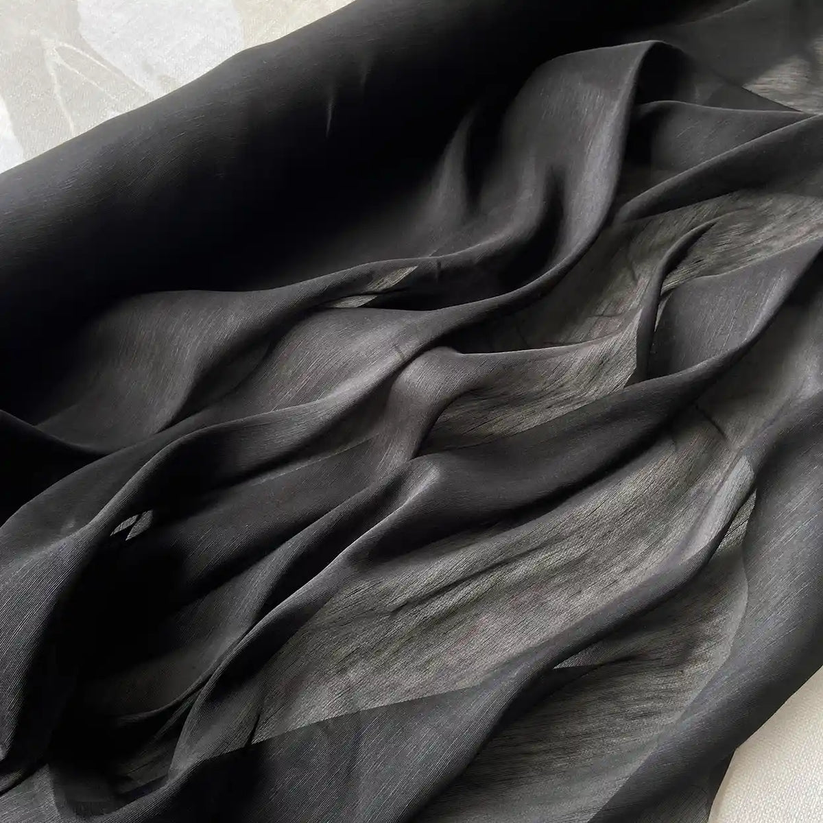 14 Momme Linen Silk Fabric by Longan Craft features sheer black Mulberry Silk in soft, flowing folds with a wavy pattern and gentle highlights. This smooth, slightly translucent organza is perfect for summer projects.