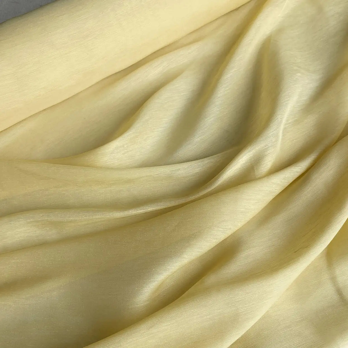 14 Momme Linen Silk Fabric by Longan Craft features pale yellow, slightly shiny material with a smooth texture. This vibrant organza mulberry silk drapes gently, creating subtle shadows—ideal for summer projects. Available by the yard.