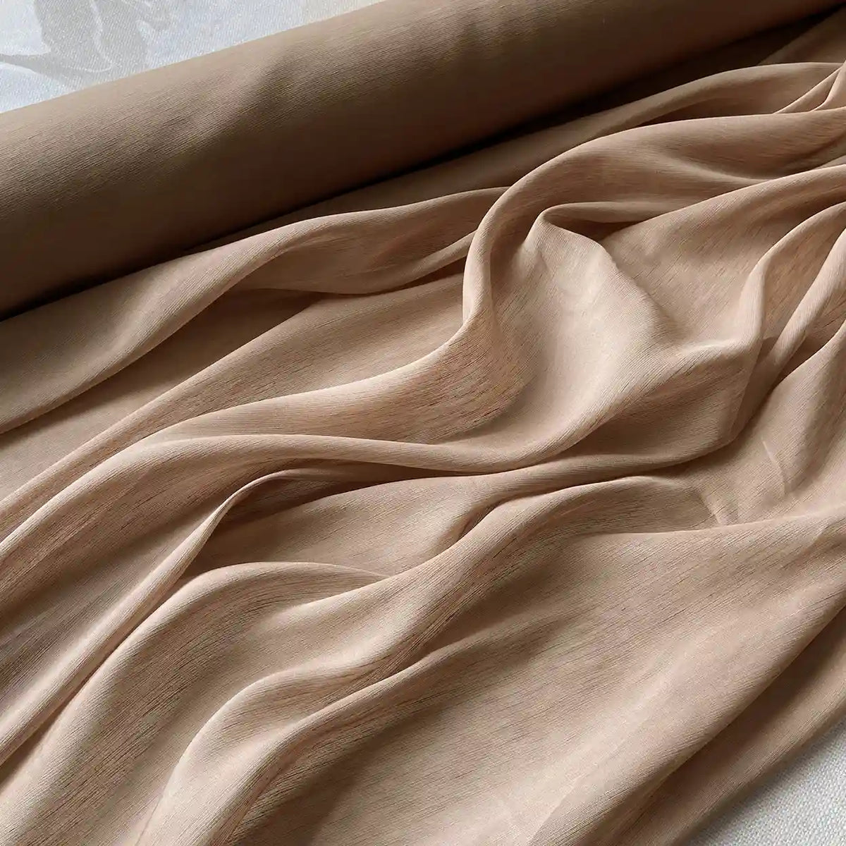 A partially unrolled roll of Longan Craft 14 Momme Linen Silk Fabric By The Yard in light beige Mulberry silk lies on a flat surface, displaying soft, flowing folds and a gently textured appearance—ideal for summer.