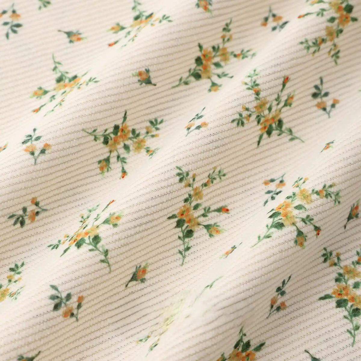Close-up of Longan Craft 16 Wale Floral Printed Corduroy Fabric by the yard, featuring a soft, textured cream base with small green leaves and yellow flowers. This premium fine wale corduroy is perfect for casual wear and craft projects.
