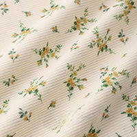 Close-up of Longan Craft 16 Wale Floral Printed Corduroy Fabric by the yard, featuring a soft, textured cream base with small green leaves and yellow flowers. This premium fine wale corduroy is perfect for casual wear and craft projects.
