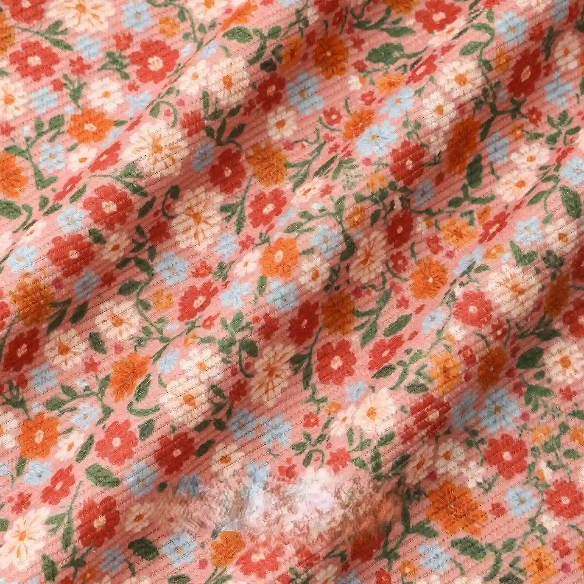 A close-up of Longan Craft's 16 Wale Floral Printed Corduroy Fabric by the yard, showing its colorful fine wale corduroy with red, orange, white, and blue flowers and green leaves on a light pink background.