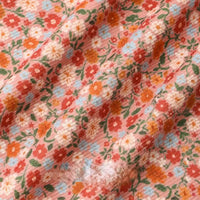 A close-up of Longan Craft's 16 Wale Floral Printed Corduroy Fabric by the yard, showing its colorful fine wale corduroy with red, orange, white, and blue flowers and green leaves on a light pink background.