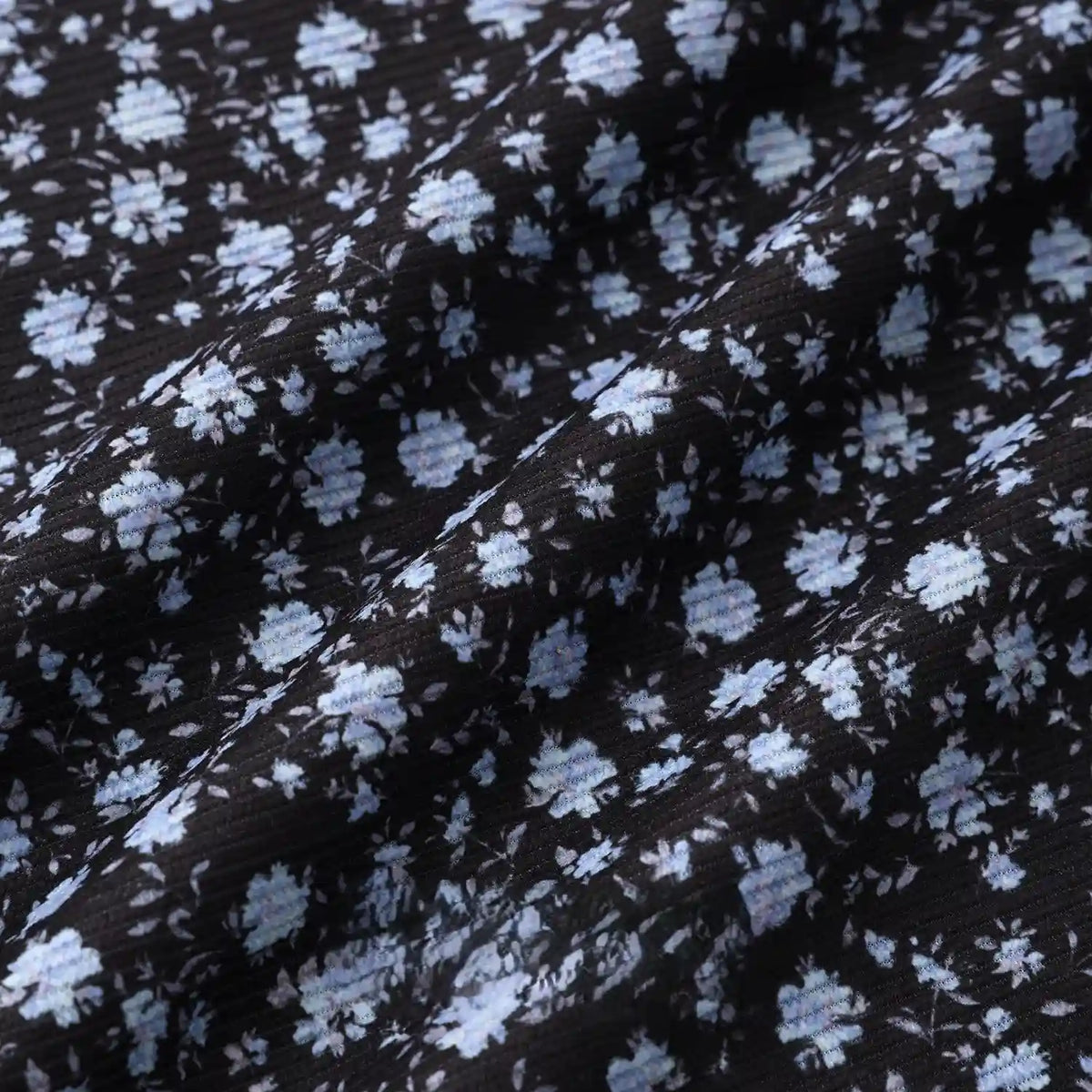 Longan Craft 16 Wale Floral Printed Corduroy Fabric by the Yard features a premium black corduroy with fine wale texture and light blue & white floral clusters, perfect for casual wear. Subtle wrinkles add depth to this colorful textile.