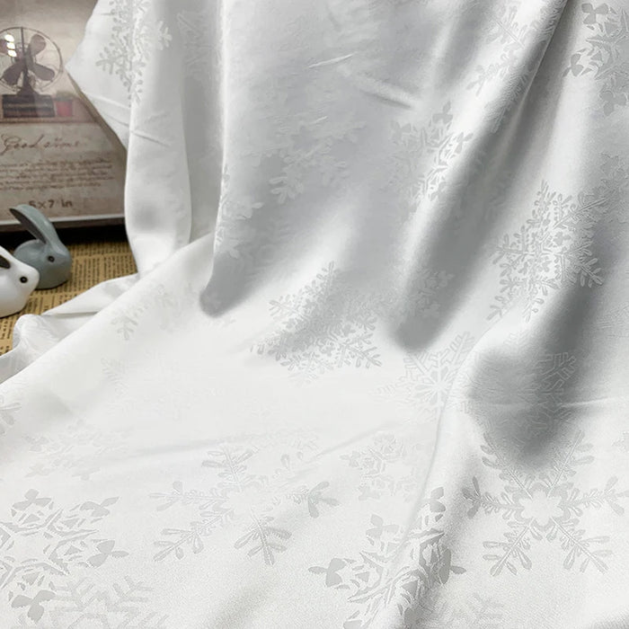 Snowflake Jacquard Satin Fabric By The Yard from Longan Craft features soft draping and delicate folds. The white polyester satin material is ideal for dresses, with a smooth texture that adds elegance to any project.